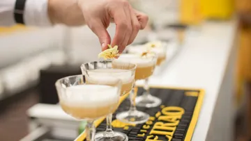 Hand garnishing cocktails with flowers on bar.