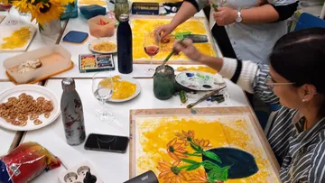 People painting sunflowers at a table with snacks.