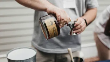 Person pouring whiskey into a jigger, outdoor setting.