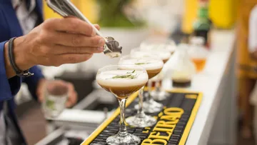 Bartender garnishing cocktails with herbs at bar.