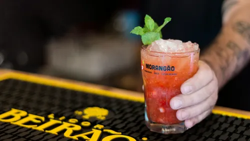 Hand holding a strawberry cocktail with mint garnish.