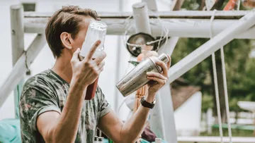 Person, die im Freien einen Cocktailshaker und eine Flasche in der Hand hält.
