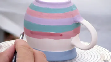 Painting colorful stripes on a ceramic mug.