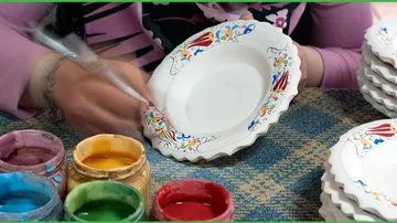 Person hand-painting ceramic plates with colorful paints.