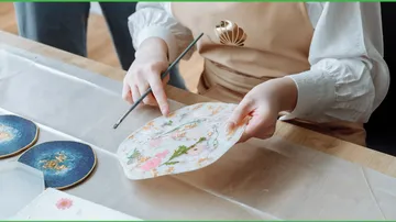 Person holding decorative paper with flowers, crafting table.