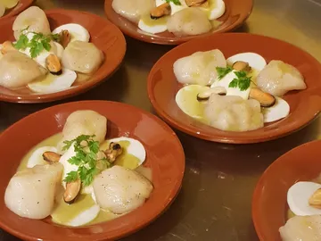 Dishes with mussels, sauce and herbs on red plates.