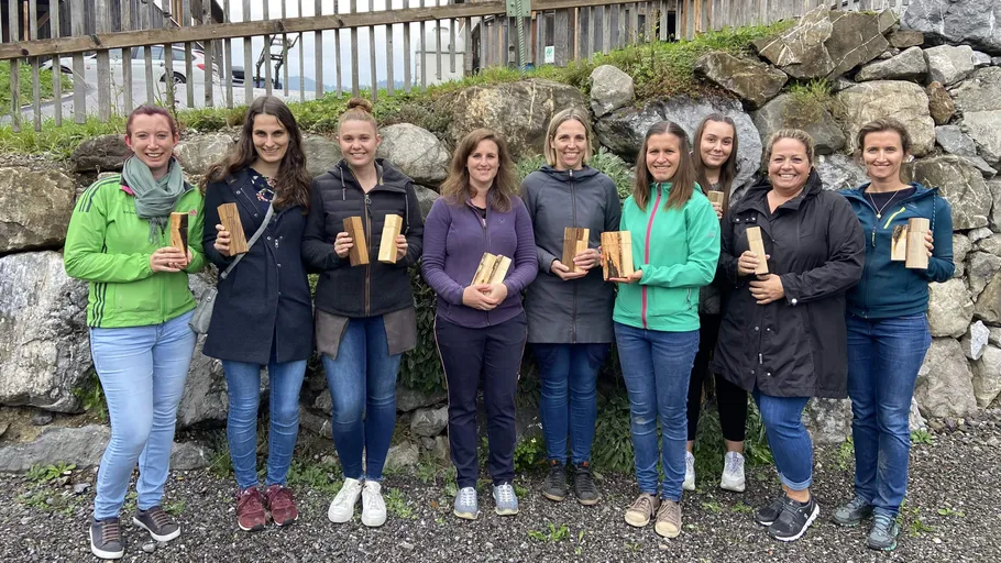 Nine women standing with wooden items outdoors.