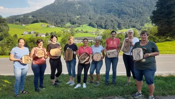 Group displaying handmade wooden clocks outdoors.