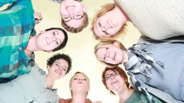 Seven people smiling in a circle, looking down.