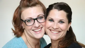 Two women smiling, close together indoors.