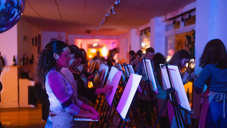 People painting on canvases in dimly lit room.