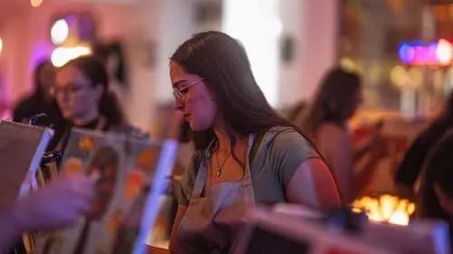 Frau, die in einer Indoor-Werkstatt malt, trägt Schürze.