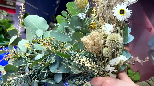 Hand holding a bouquet of mixed greenery.