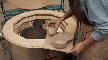 Person, die Keramikschalen in den Ofen stellt.