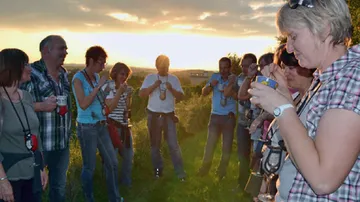 Gruppe von Menschen, die draußen Wein bei Sonnenuntergang probieren.