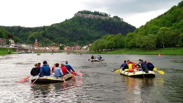Groups of people rafting on a river, surrounded by green hills.