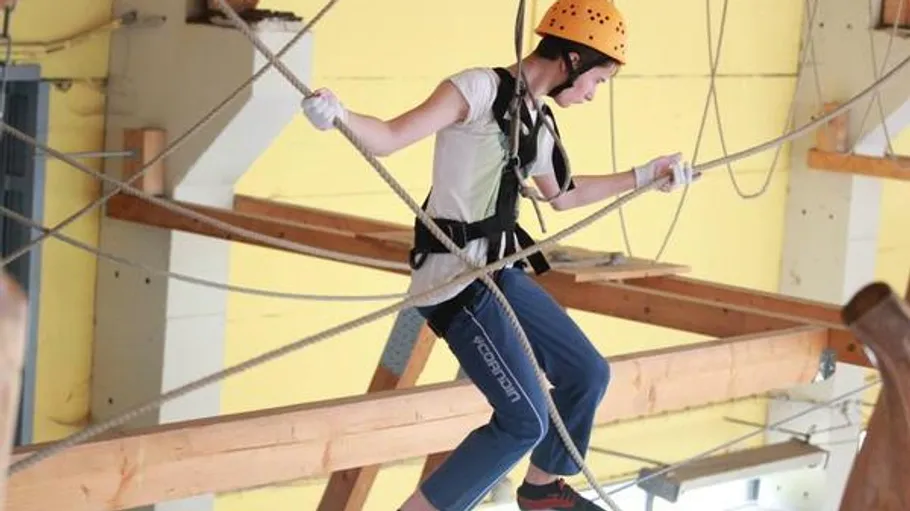 Person traversing ropes course indoors.