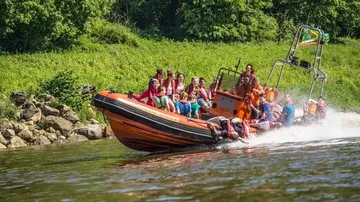 Menschen in einem orangefarbenen Boot auf einem Fluss in der Nähe von viel Grün.