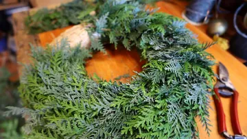 Grüner Kranz auf einem Holztisch, Gartenschere in der Nähe.