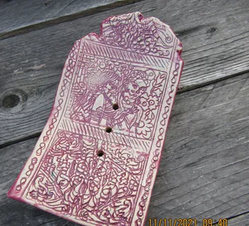 Decorative ceramic plaque with intricate pink design.