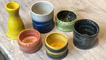 Bunte Keramikbecher auf einem Holztisch.