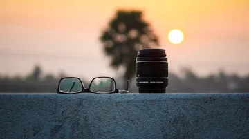 Glasses and camera lens on wall at sunset.