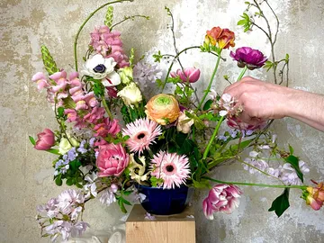 Colourful flowers are arranged in a vase by one hand.
