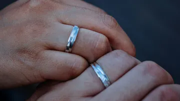 Two hands with silver rings, clasped together.