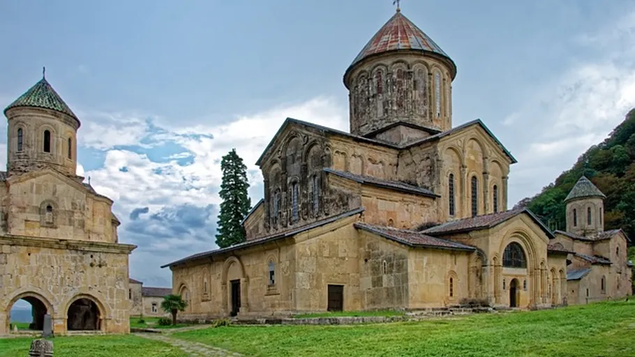 Ancient stone monastery with towers in lush setting.