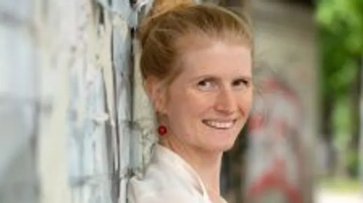 Person smiling near graffiti-covered wall outdoors.