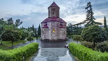 Small church with red roof in garden setting.