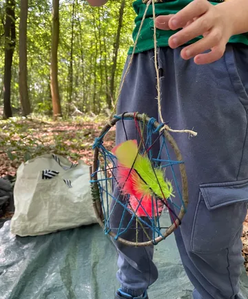 Kind hält einen handgefertigten Traumfänger im Wald in der Hand.