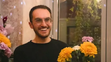 Smiling person with flowers indoors.