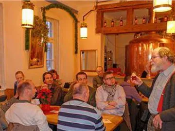 Mann mit Bier spricht zu Gästen in gemütlichem Brauhaus.