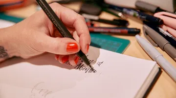 Hand writing calligraphy with pen on paper.