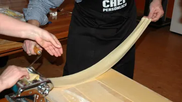 Hände, die Nudelteig mit der Maschine ausrollen.