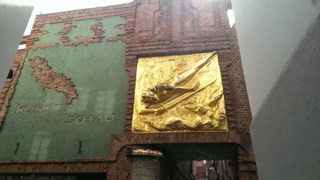 Gold sculpture of a man on a brick wall.