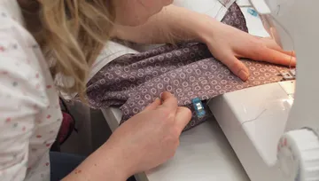 A person sews fabric using a sewing machine.