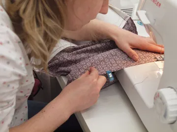 A person sews fabric using a sewing machine.