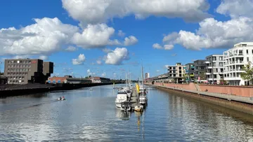 Boats docked in a modern canal under blue sky.