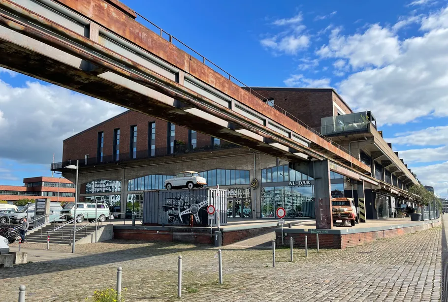 Backsteingebäude mit Oldtimern und Bahngleisen.