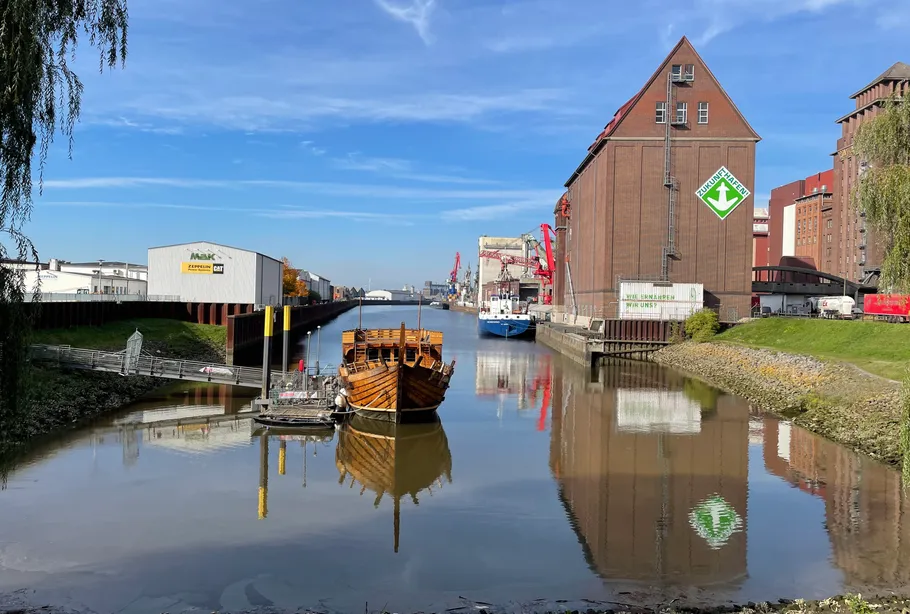Holzschiff, das im Industriehafen mit Lagerhäusern angedockt ist.