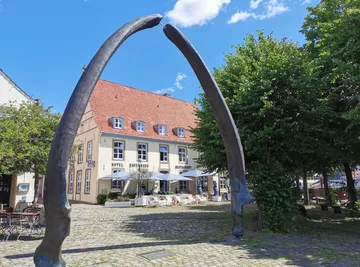 Large whale bone sculpture near trees and building.