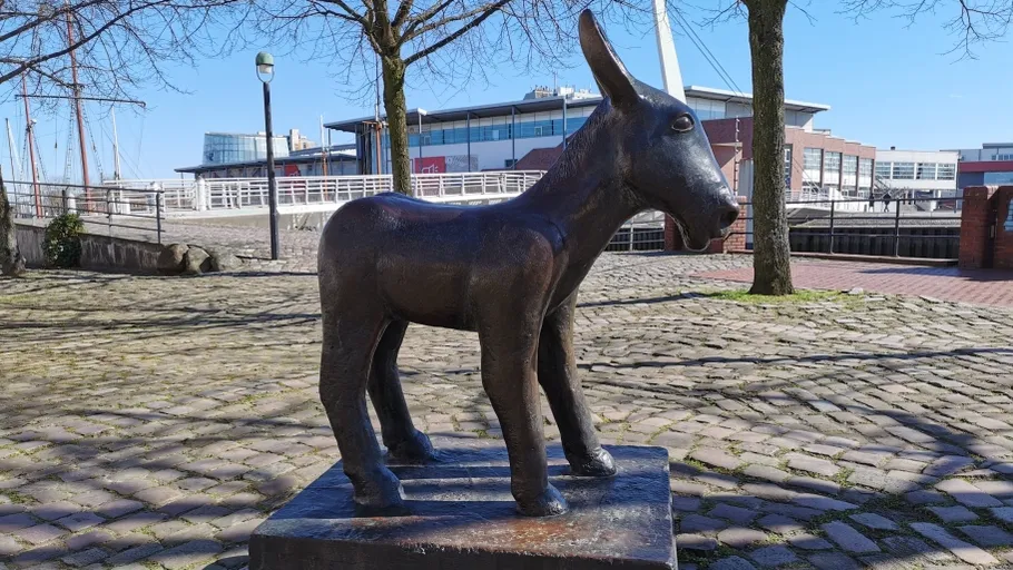 Bronze donkey statue on cobblestone street.