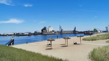 Sand beach with umbrellas, industrial port in background.