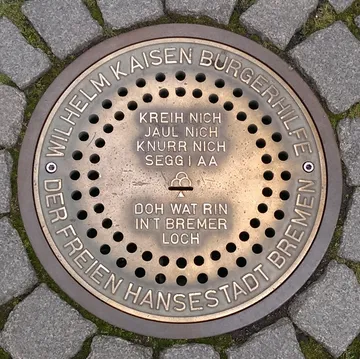 Runder Kanaldeckel mit Text und kleinen Löchern.