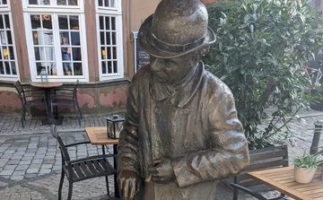 Bronze statue of man with cane in outdoor cafe.