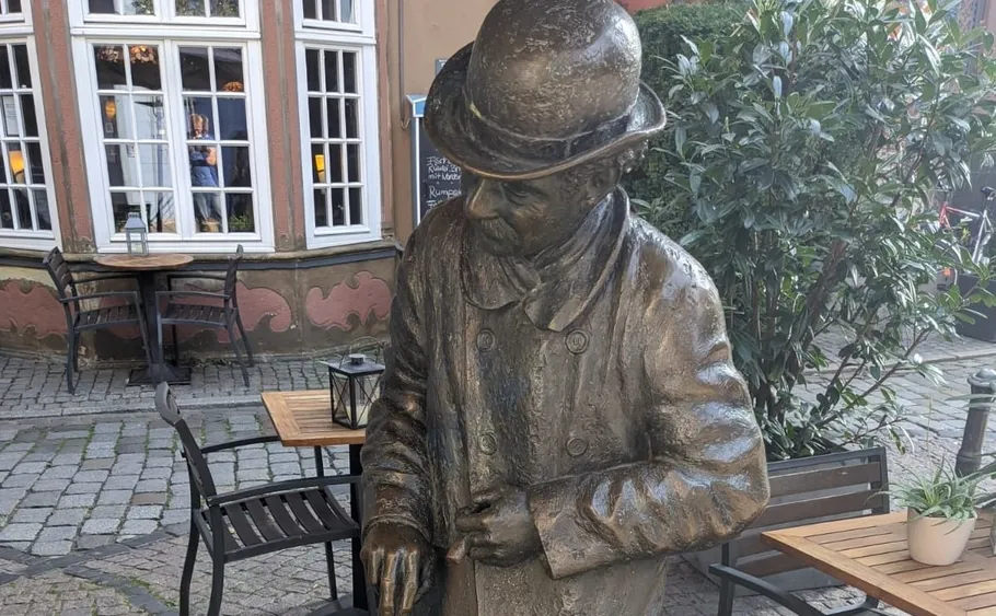 Bronzestatue eines Mannes mit Stock im Café im Freien.