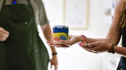 Hände, die eine bunt gestreifte Tasse halten.