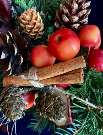 Cinnamon sticks and apples with pinecones on greenery.
